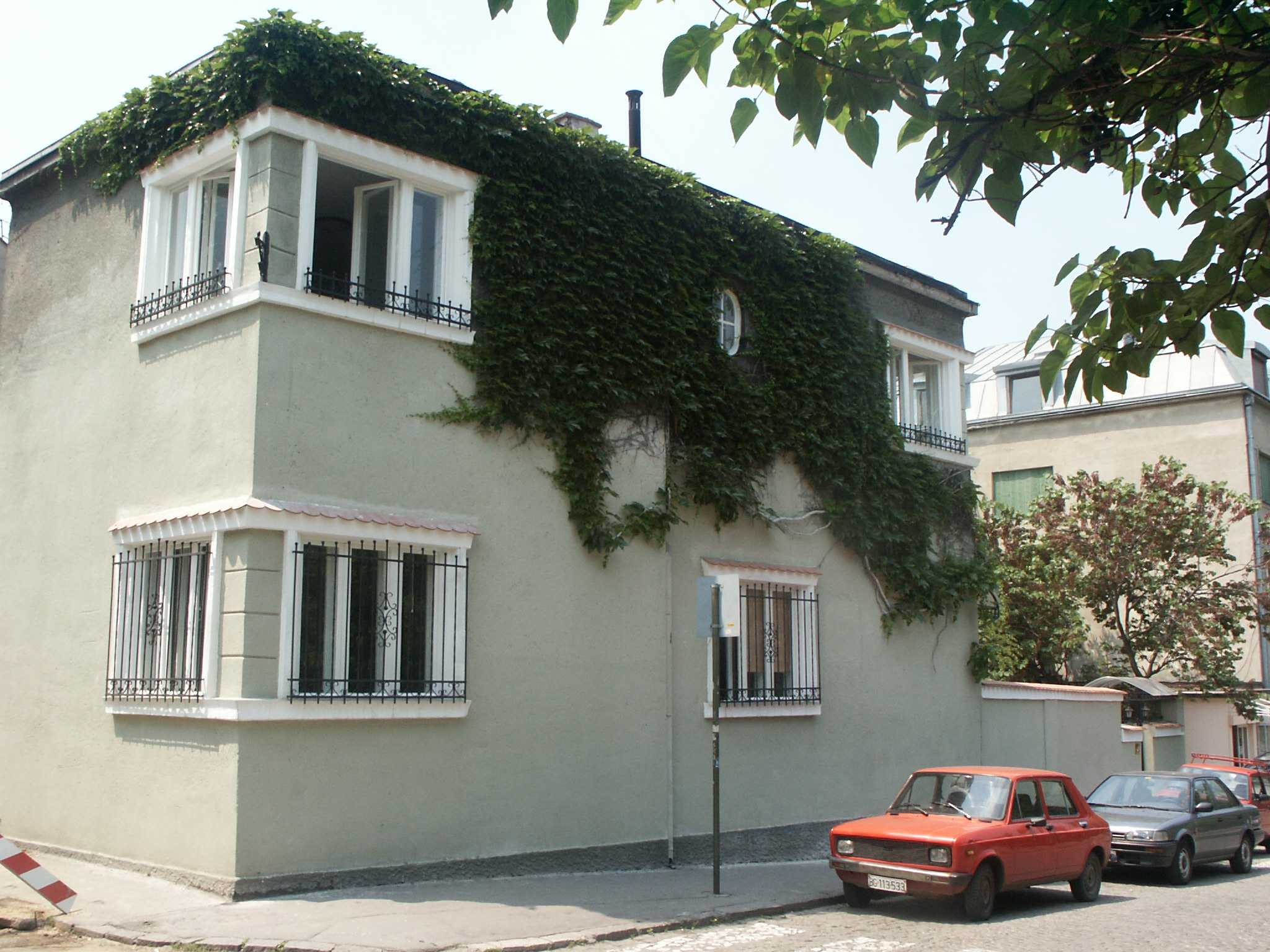 Two-story stucco building covered in green ivy with barred windows, bright afternoon sun
